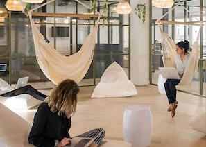 A modern lounge area with seating options including a hammock and bean bags, a large vase, and a laptop on a table. - Student Only Non Ensuite Room Ivy Halls (London)
