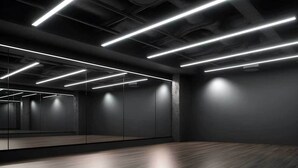 A modern, dimly lit room with a large mirror, wooden flooring, and linear ceiling lights. - Student Only Non Ensuite Room Ivy Halls (London)