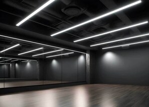 A modern, dimly lit room with a large mirror, wooden flooring, and linear ceiling lights. - Student Only Non Ensuite Room Ivy Halls (London)
