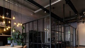 A modern office space with glass partitions, hanging light bulbs, and a round table with chairs. - Student Only Non Ensuite Room Ivy Halls (London)