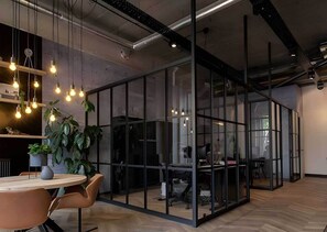 A modern office space with glass partitions, hanging light bulbs, and a round table with chairs. - Student Only Non Ensuite Room Ivy Halls (London)