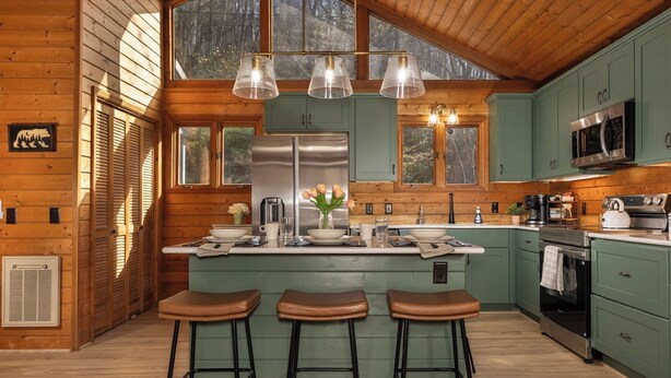 Interno di una casetta in legno con isola della cucina, sgabelli da bar e un'ampia finestra.