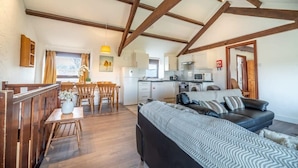 A cozy room with a sofa, wooden dining table, and a kitchen area with appliances. - 3 Neighbouring Holiday Cottages nr Bude, Sleeps 14 (Bude)