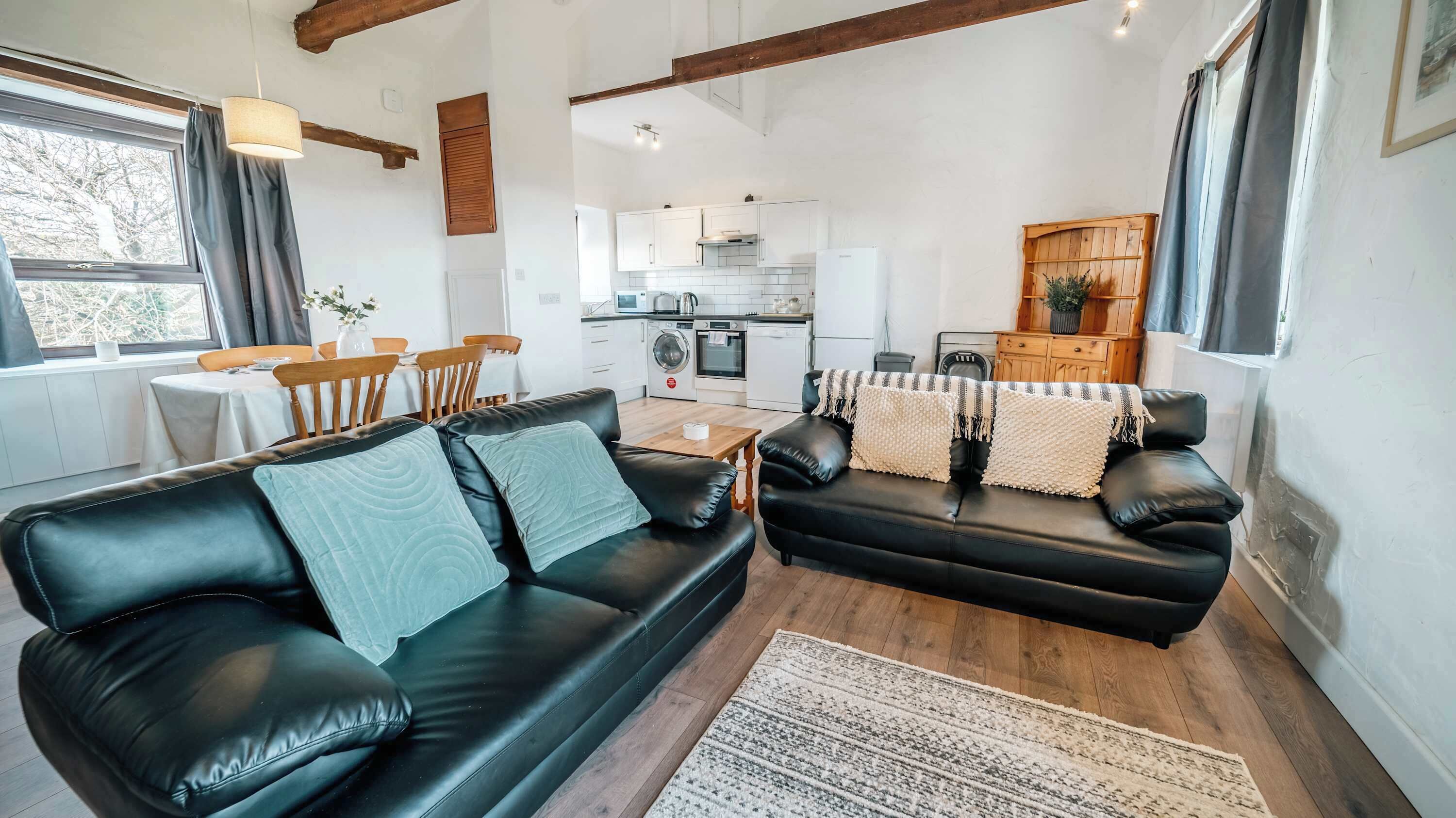 Ein modernes Wohnzimmer mit einer schwarzen Ledersofa, einem Essbereich mit Holzsesseln und einer Küche mit weißen Schränken.