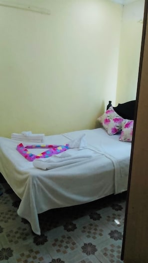 Una cama con ropa de cama blanca, una toalla colorida y almohadas estampadas.