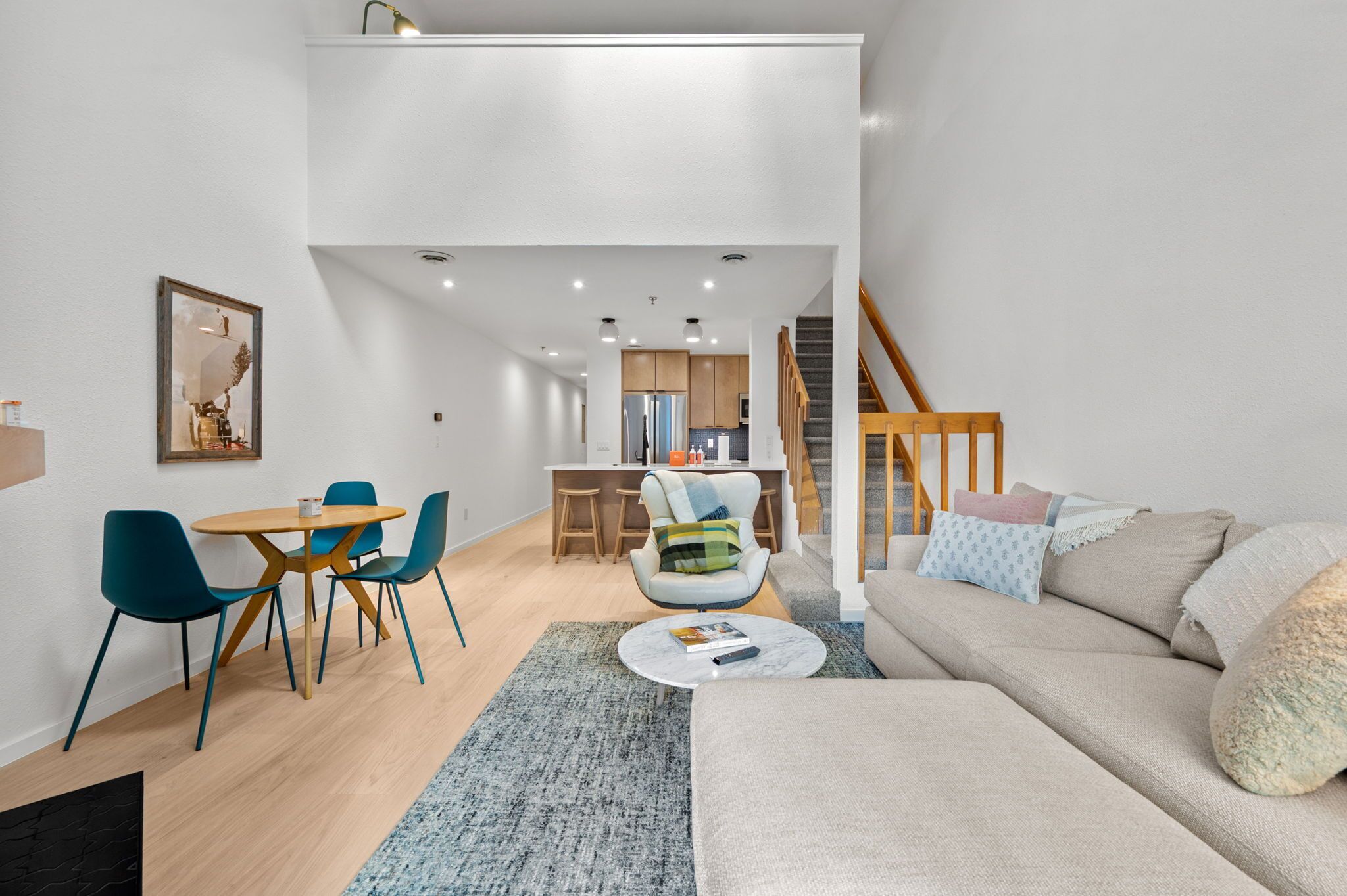 En moderne stue med sofa, spisebord med stole, et køkken og en trappe.