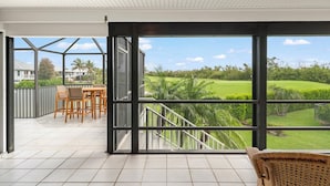 Un espacio al aire libre cubierto con vista a un campo de golf, una mesa de comedor con sillas y una silla de mimbre.