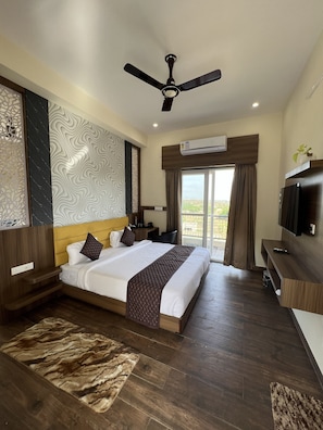 A hotel room with a bed, a ceiling fan, an air conditioning unit, a TV, and a view of the outdoors. - Kapish Farms by Kavya International (Udaipur)