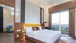 A modern hotel room with a large bed, a balcony with a view, and a blue chair. - Kapish Farms by Kavya International (Udaipur)