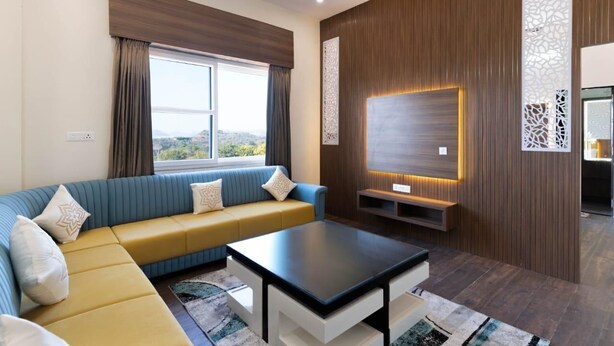 A modern living room with a sofa, coffee table, and a TV mounted on a wooden wall. - Kapish Farms by Kavya International (Udaipur)