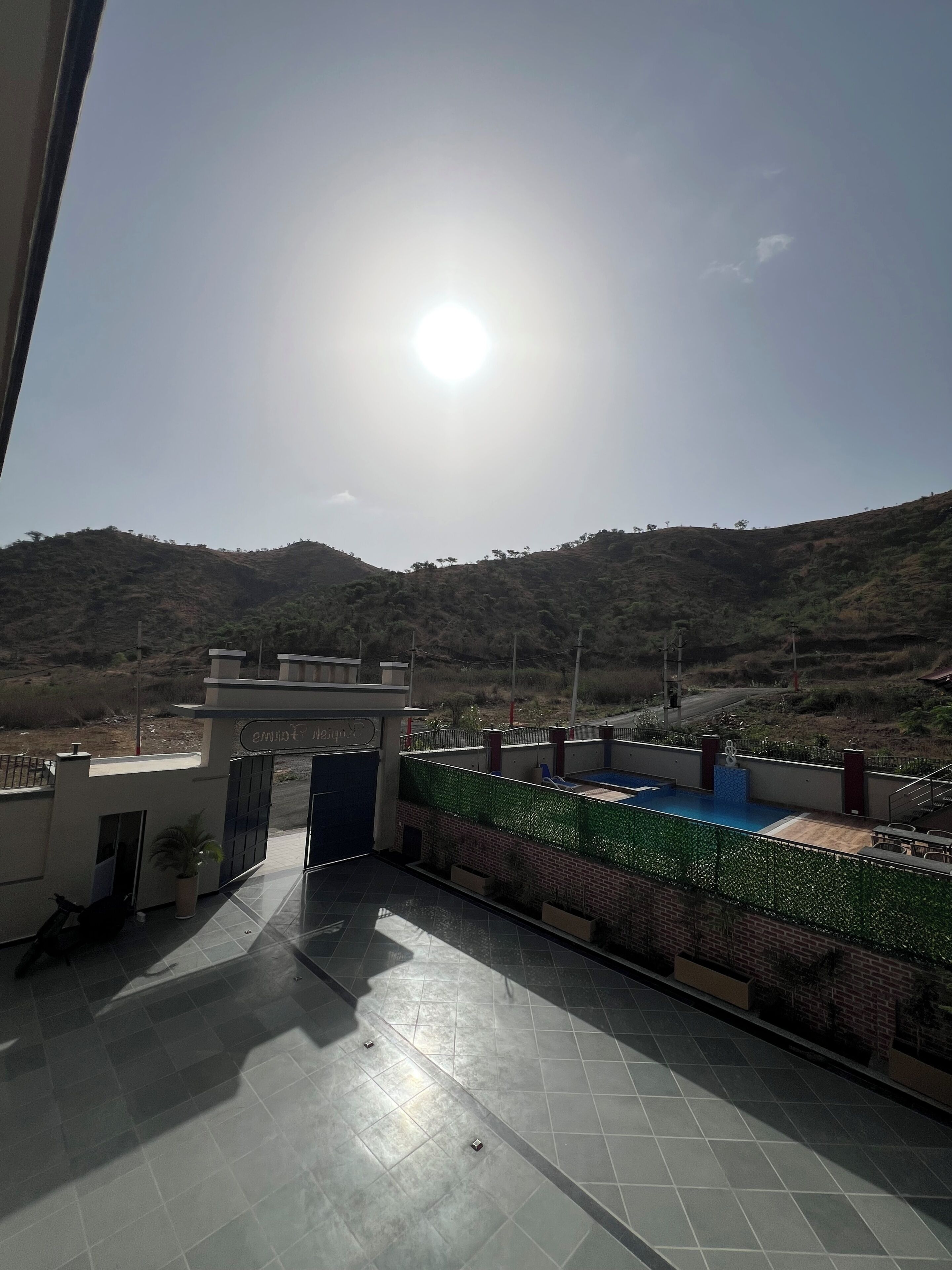A rooftop terrace with a view of a hilly landscape, a gated entrance, and a pool area.