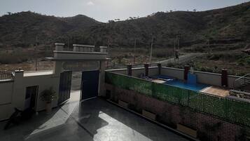 A rooftop terrace with a view of a hilly landscape, a gated entrance, and a pool area.