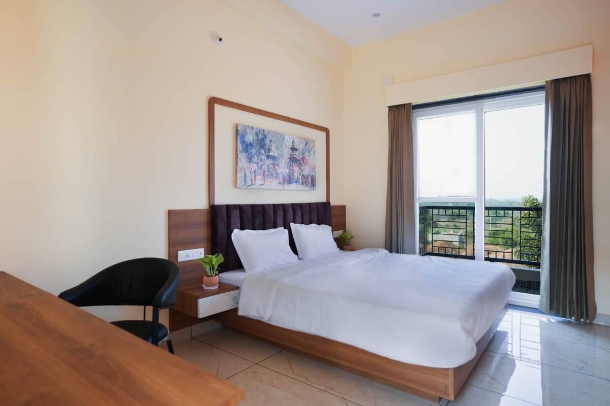 Habitació d'hotel amb llit, escriptori, cadira, un quadre a la paret i un balcó amb vistes.