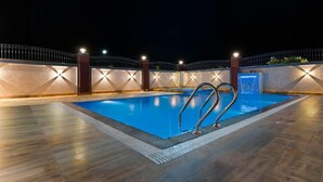A swimming pool with a metal ladder, surrounded by a low wall with lights, at night. - Kapish Farms by Kavya International (Udaipur)