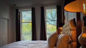 Een slaapkamer met een groot bed, een nachtkastje, een lamp en een raam met gordijnen.