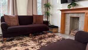 Een woonkamer met een donkergrijze bank, een open haard, een televisie en een raam met gordijnen.