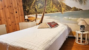 Camera da letto con un murale a tema spiaggia, un letto con copriletto trapuntato, un comodino con lampada e una cassettiera.