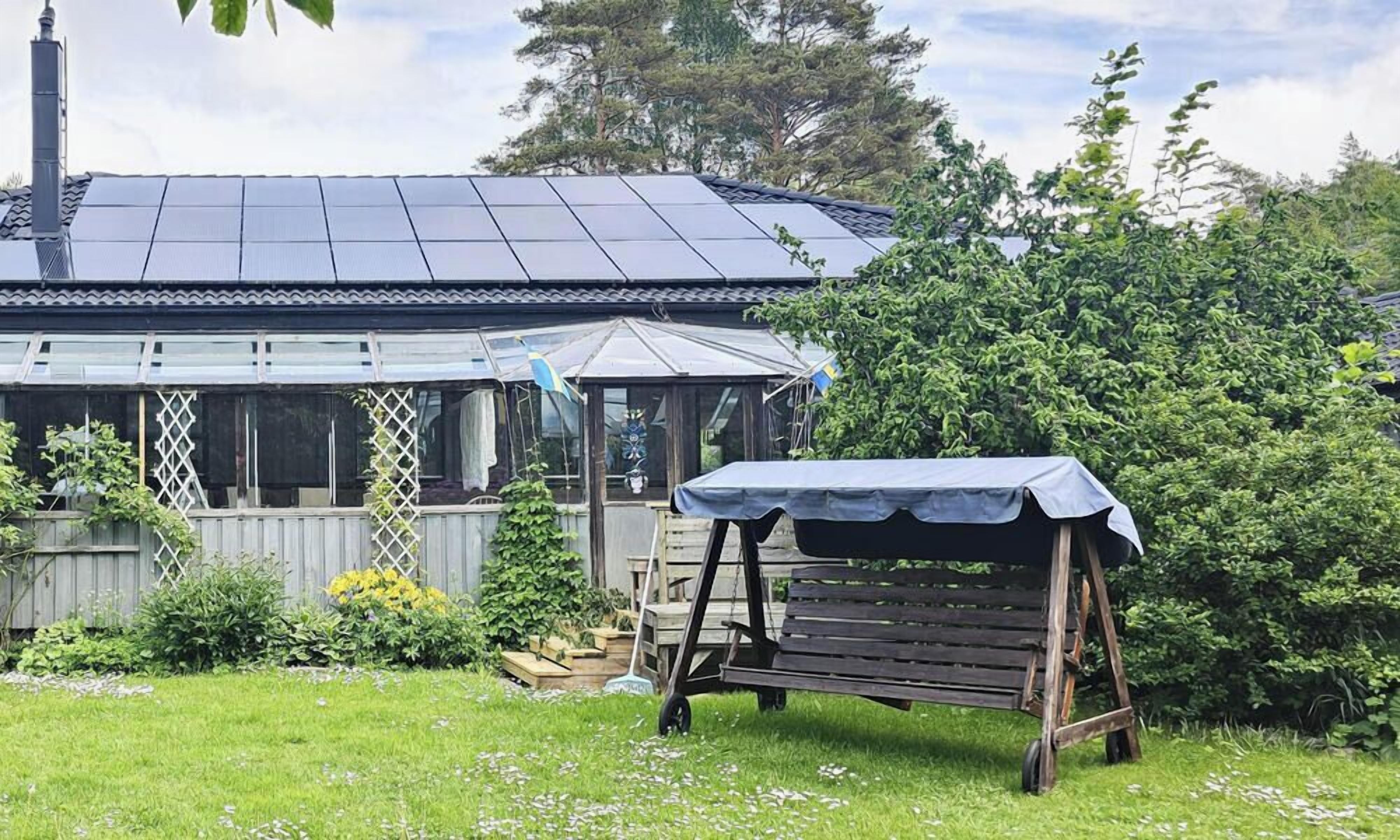 Ett hus med solpaneler på taket, en inglasad uteplats och en träbänk.