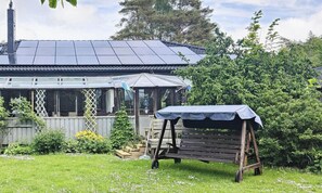 Ein Haus mit Solardach, überdachter Terrasse und Holzbank.