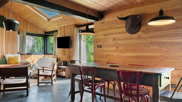 Un intérieur en bois comprenant un coin repas, un téléviseur fixé au mur et une grande fenêtre.