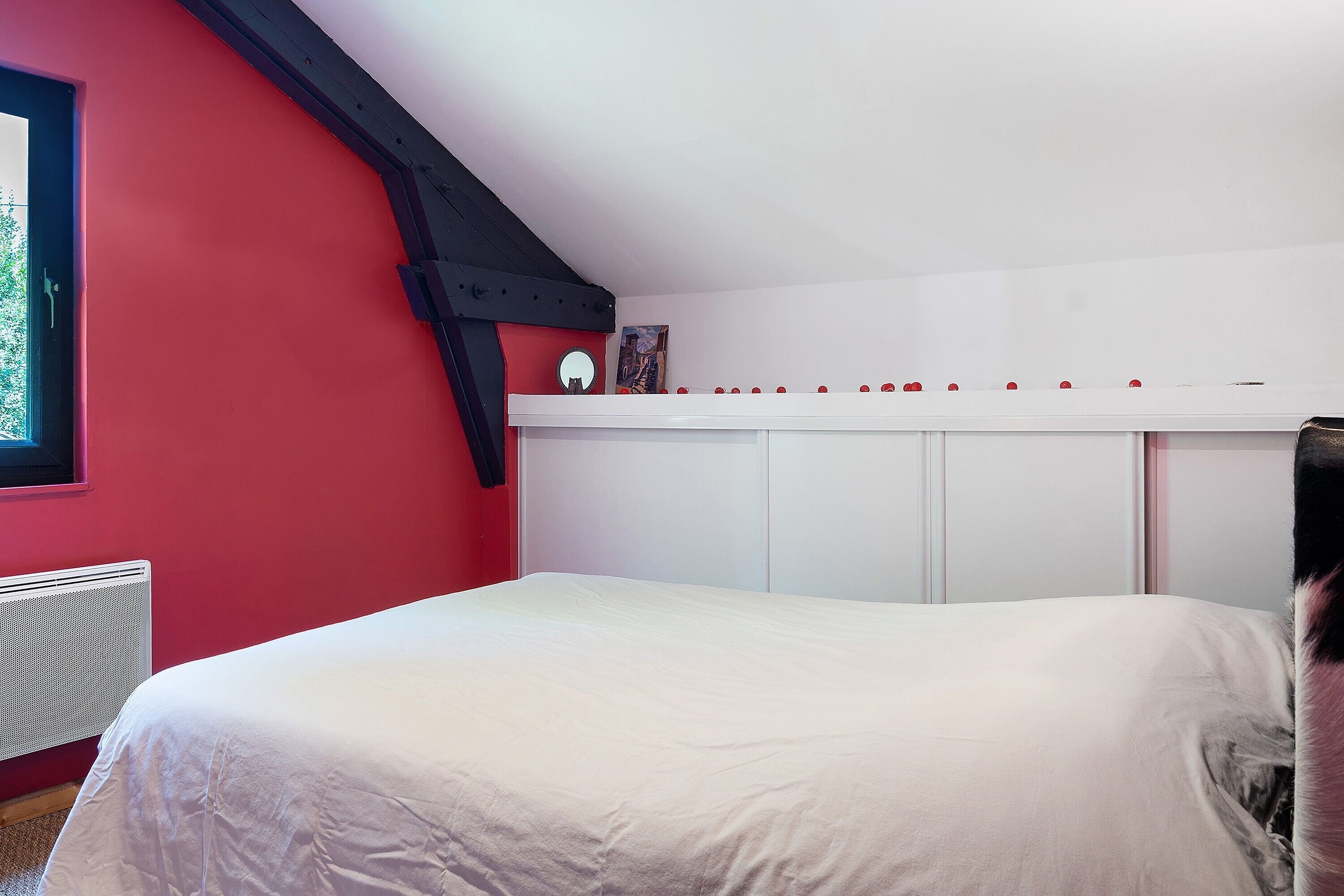 A bedroom with a bed, a radiator, a window, and a white wardrobe.