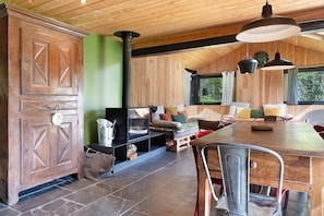 L’intérieur d’un chalet rustique est aménagé avec une table à manger en bois, des chaises en métal, un canapé et une cheminée.
