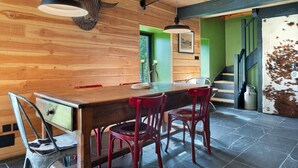 Une table à manger en bois, des chaises, un luminaire suspendu et un escalier menant à une pièce aux murs verts.