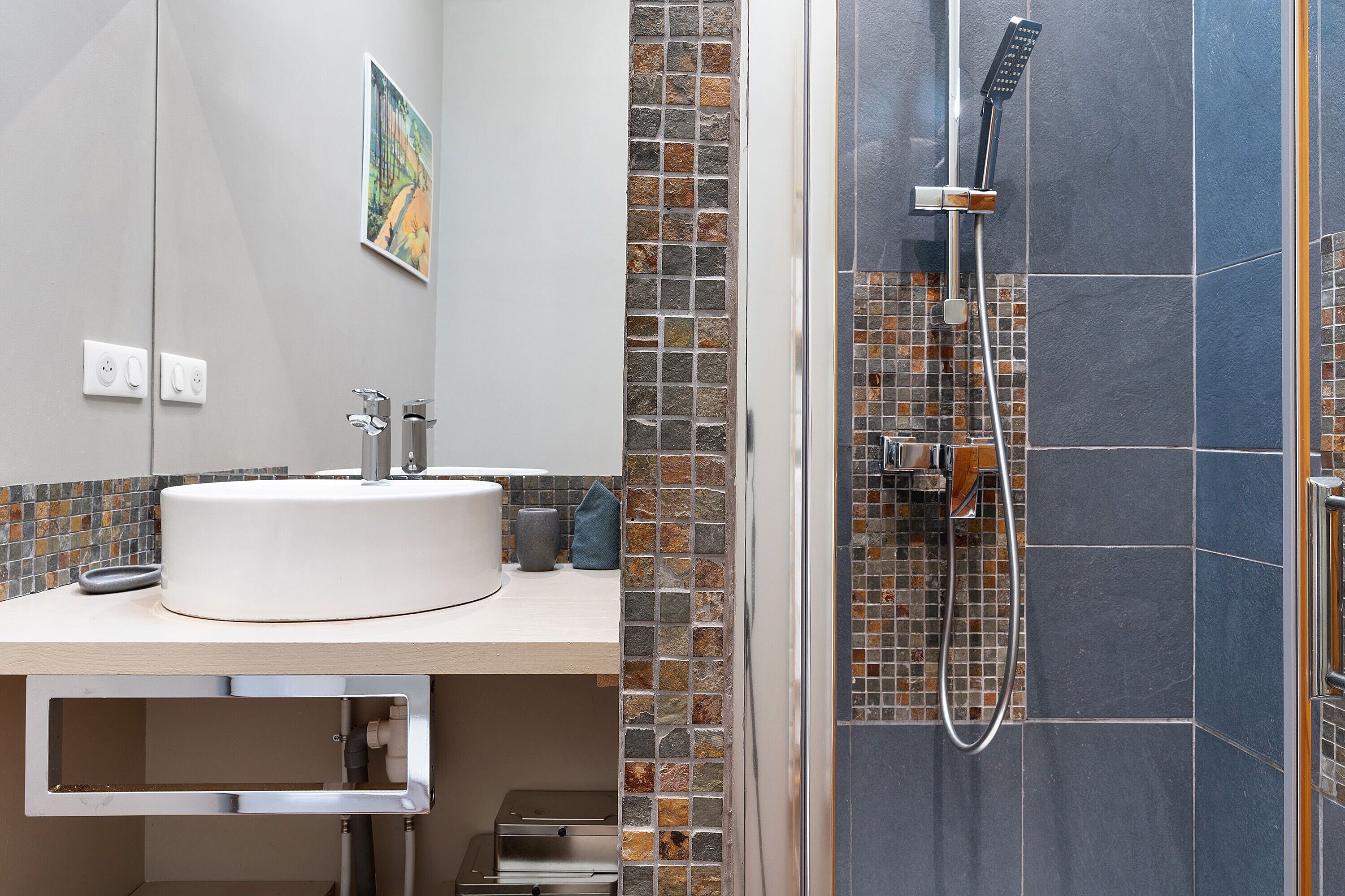 A bathroom with a round sink, a shower with a handheld showerhead, and a mosaic tile wall.