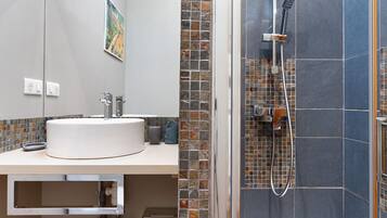 Et badeværelse med en rund vask, en bruser med håndbruser og en væg med mosaikfliser.