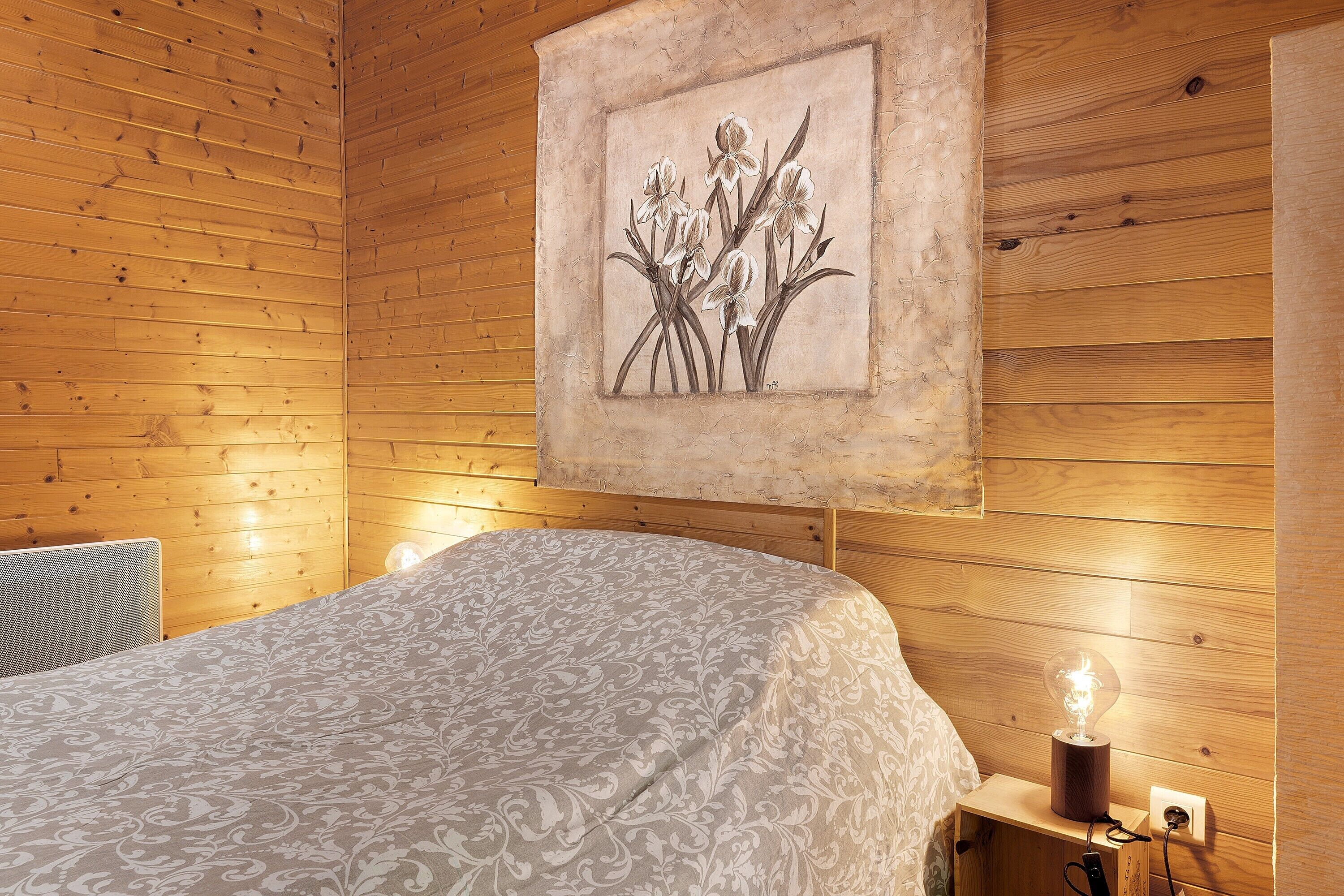 A wooden-paneled room with a bed, a framed artwork, and a bedside lamp.
