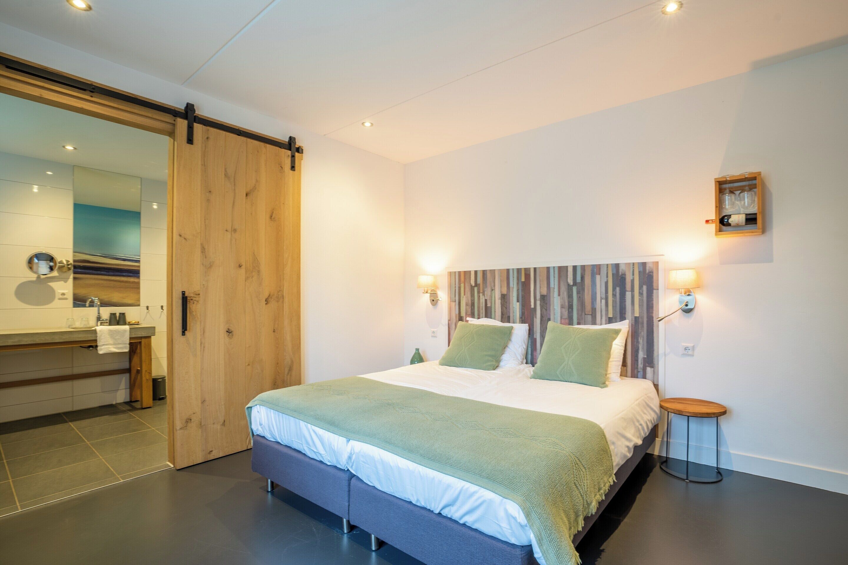 Quarto moderno com uma cama grande, uma porta deslizante de madeira, uma mesinha de cabeceira e um aplique de parede.