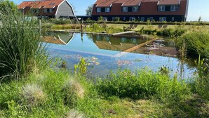 Ein Wohngebiet mit Teich, einem Haus mit rotem Dach und einem großen, weißen Gebäude.