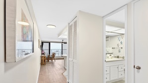 Um corredor com área de jantar, um armário com portas venezianas e um banheiro com pia branca e piso ladrilhado.