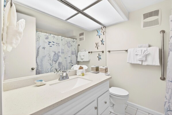 A bathroom with a large mirror, a sink, a toilet, and a shower curtain with a marine theme. - Simple Condo Great View (Lahaina)