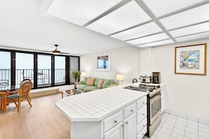 Eine moderne Küche mit einer großen Kochinsel, einem Essbereich mit Korbstühlen, einer Couch und Blick durch große Fenster.