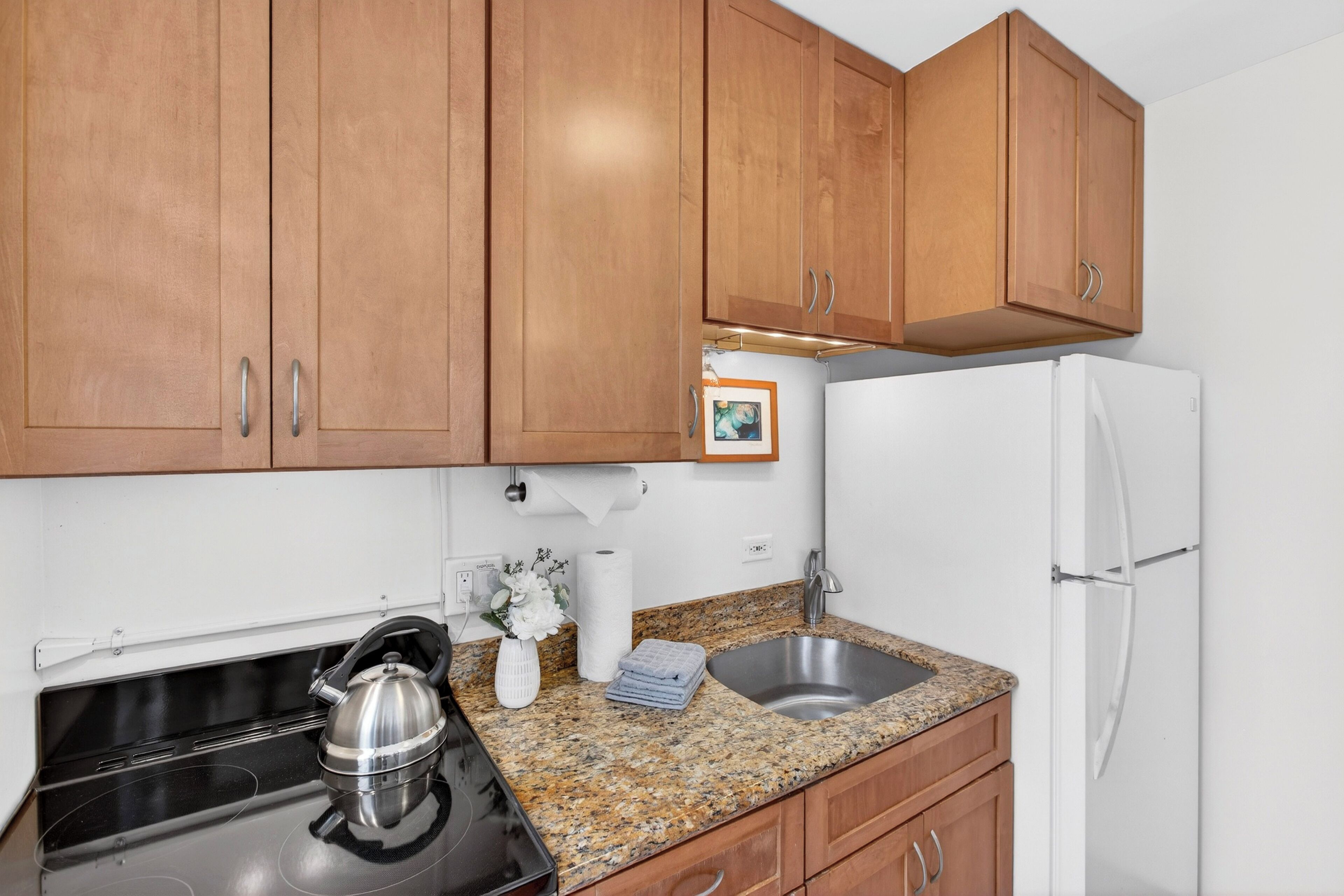 A kitchen with wooden cabinets, a stainless steel sink, a white refrigerator, and a stove.