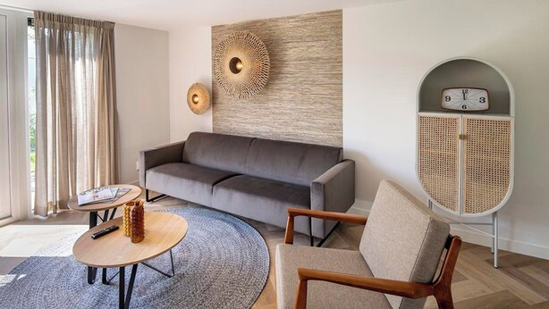 A modern living room with a sofa, a round coffee table, a wooden chair, a rattan sideboard, and a wall clock. - Coastal Home With Sauna for 6 (Sint Maarten)