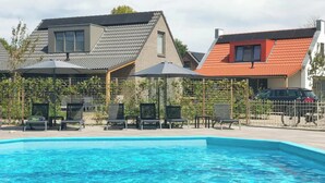 A swimming pool with lounge chairs and umbrellas, surrounded by houses with distinct roof colors. - Coastal Home With Sauna for 6 (Sint Maarten)