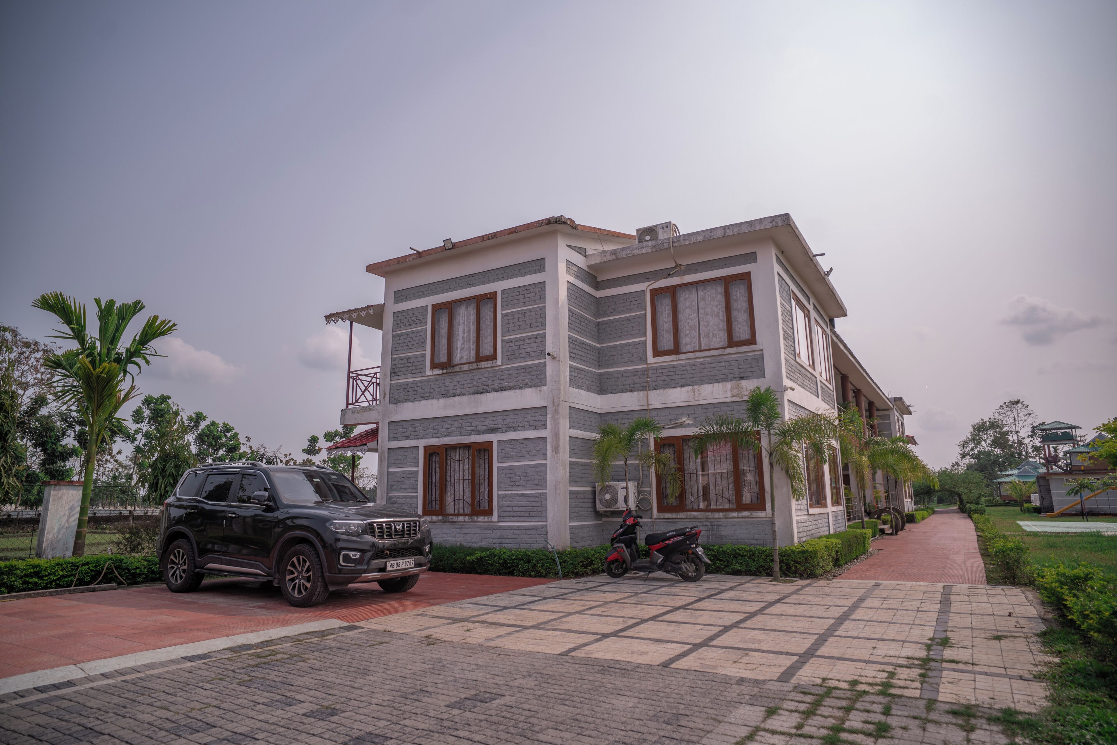 A modern two-story building with a paved driveway, parked vehicles, and surrounding greenery.