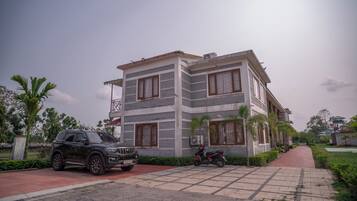A modern two-story building with a paved driveway, parked vehicles, and surrounding greenery.