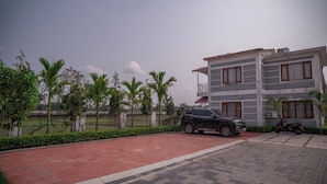 A multi-story building with a paved driveway, a parked SUV, and a scooter. - Resort Bihanga (Mal)