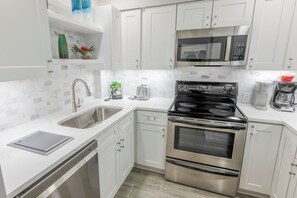 A modern kitchen with white cabinets, a stainless steel stove, a microwave, and a dishwasher. - 112 Arrowhead – Unique Lakefront 2BR at Kingston (Myrtle Beach)