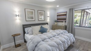 A bedroom with a bed, bedside tables, wall-mounted lights, and a window with curtains. - 112 Arrowhead – Unique Lakefront 2BR at Kingston (Myrtle Beach)