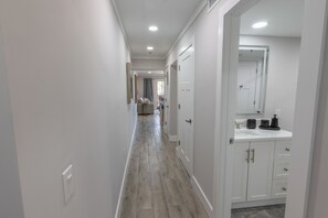 A hallway with a wooden floor, white walls, and a kitchen area with white cabinets and a countertop. - 112 Arrowhead – Unique Lakefront 2BR at Kingston (Myrtle Beach)
