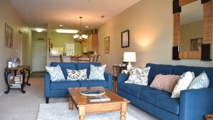 A living room with a blue sofa, a wooden coffee table, and a chandelier. - New 2026 Listing! Pond View Condo in Five Points (Lewes)