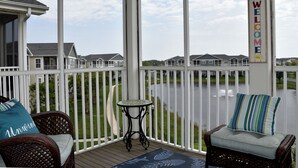 A covered porch with wicker furniture, a small table, and a view of houses across a body of water. - New 2026 Listing! Pond View Condo in Five Points (Lewes)