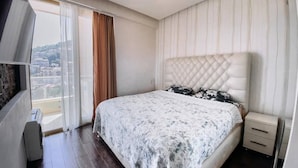 Un dormitorio con cama, mesita de noche, ventana con cortinas y vistas al exterior.