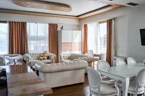 A modern living room with a sofa set, a dining table with chairs, and a large window with curtains. - Penthouse sea view with pool on terrace (Budva)
