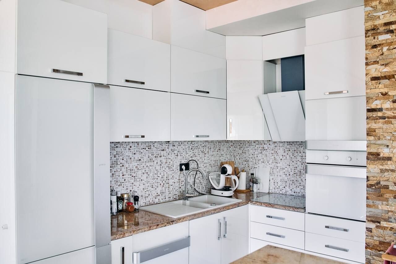 A modern kitchen with white cabinetry, a tiled backsplash, and a granite countertop.