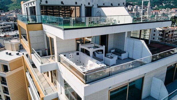 Un edificio de varios pisos con terraza en la azotea, que cuenta con asientos al aire libre y un jacuzzi.
